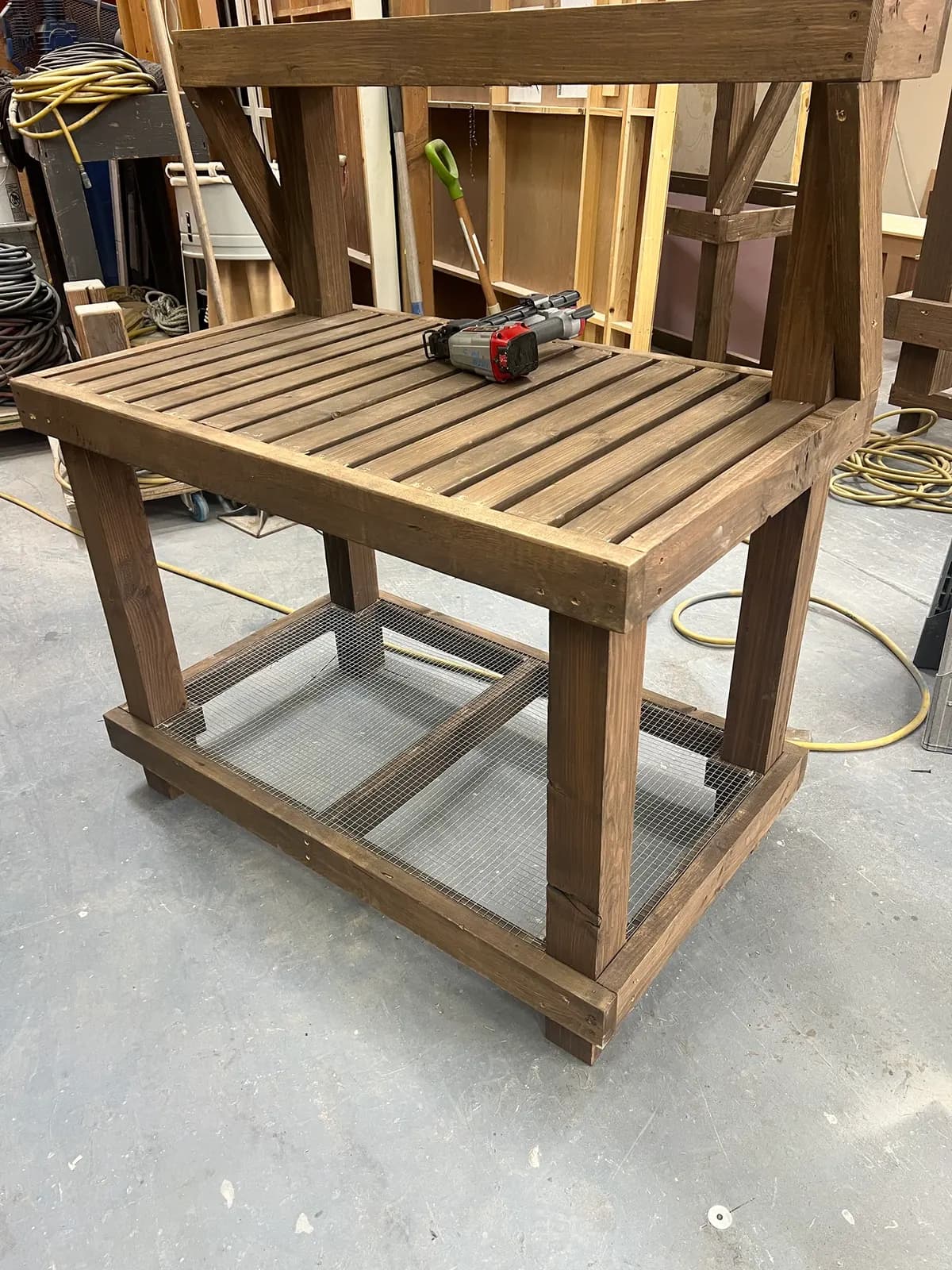 A finished bench module in the shop: stained wood, slatted top, wire-mesh lower shelf, and braced posts