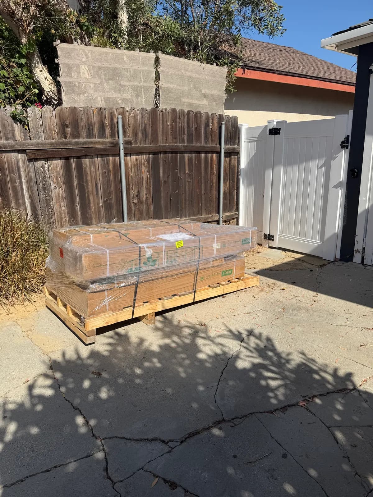 The Vego greenhouse kit delivered on a shrink-wrapped pallet beside the side gate