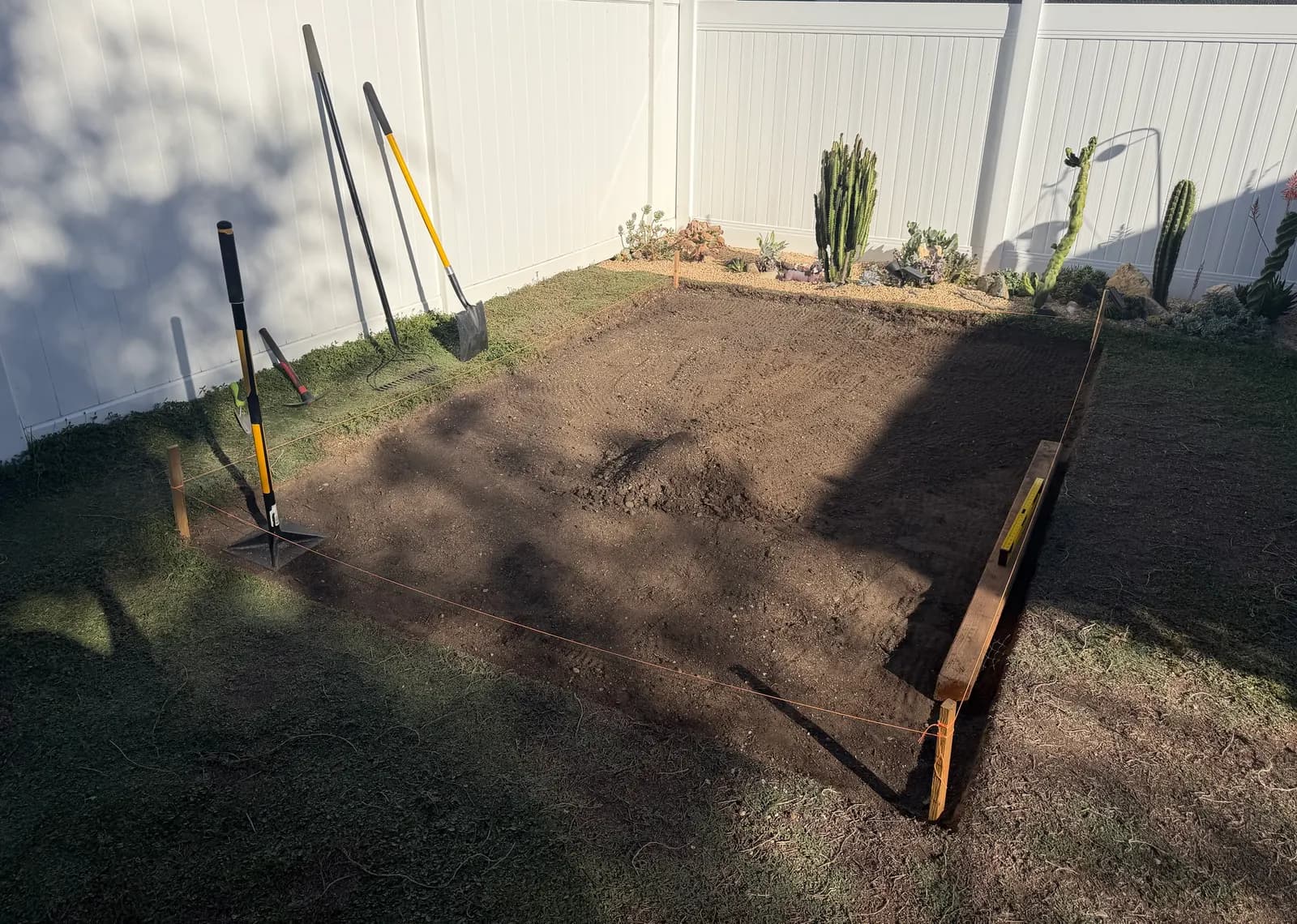 The raked pad with a hand tamper, and a 6×6 timber and level along one edge