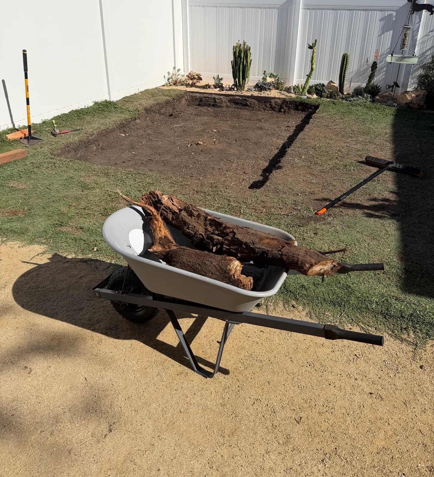 A wheelbarrow of old tree roots dug out of the pad, the excavated footprint behind it