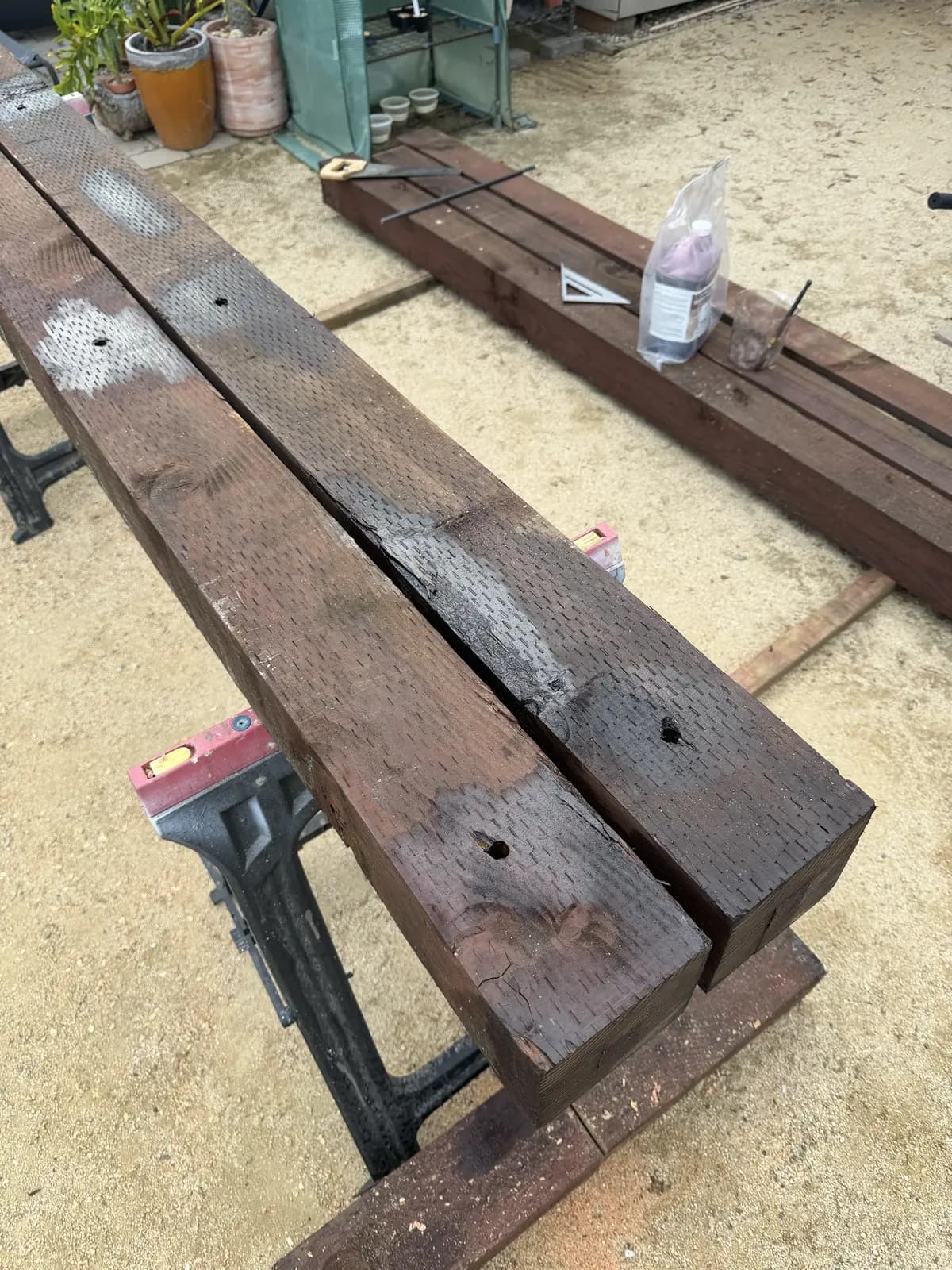 Two drilled 6×6 timbers on sawhorses with fresh preservative brushed around the holes and cut ends